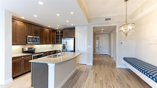 kitchen featuring light stone countertops, appliances with stainless steel finishes, sink, pendant lighting, and light hardwood / wood-style flooring