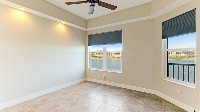 empty room with ceiling fan, a water view, and light tile patterned floors