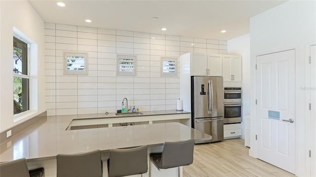 kitchen featuring light wood-type flooring, a breakfast bar, stainless steel appliances, sink, and white cabinetry