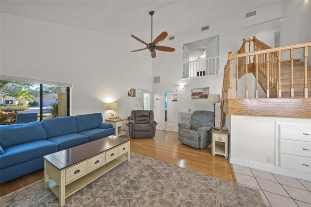 living room featuring ceiling fan, a towering ceiling, a healthy amount of sunlight, and wood-type flooring