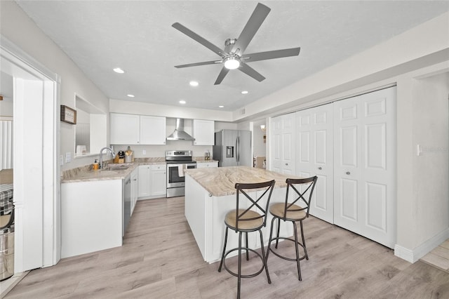 kitchen with appliances with stainless steel finishes, light wood-type flooring, a kitchen island, and wall chimney exhaust hood