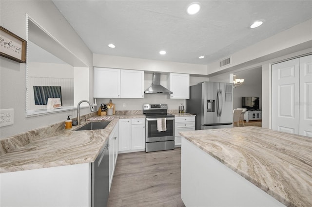 kitchen with appliances with stainless steel finishes, white cabinetry, wall chimney exhaust hood, and sink