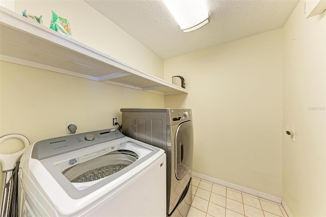 clothes washing area with light tile patterned floors, washer and dryer, and a textured ceiling