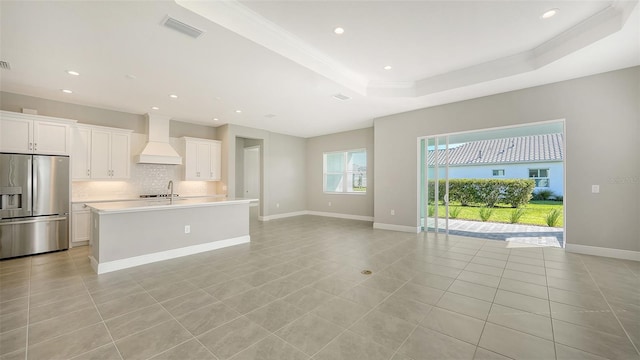 kitchen featuring white cabinetry, stainless steel fridge with ice dispenser, a kitchen island with sink, and custom exhaust hood