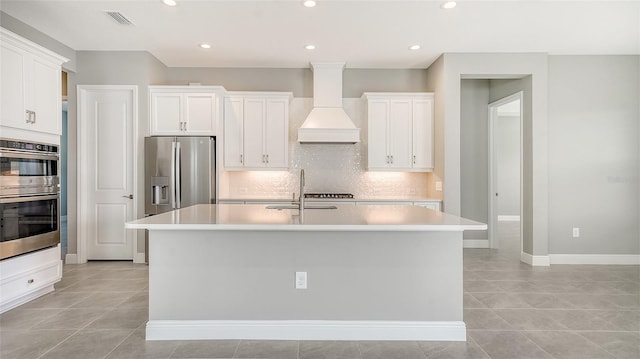 kitchen with premium range hood, a center island with sink, white cabinets, and appliances with stainless steel finishes