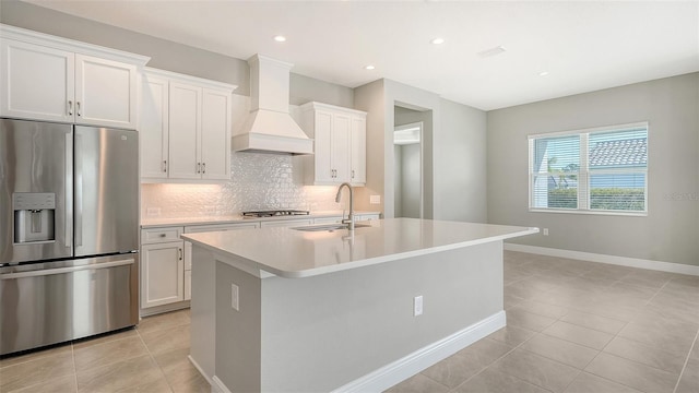 kitchen featuring custom range hood, stainless steel appliances, white cabinets, an island with sink, and light tile patterned flooring