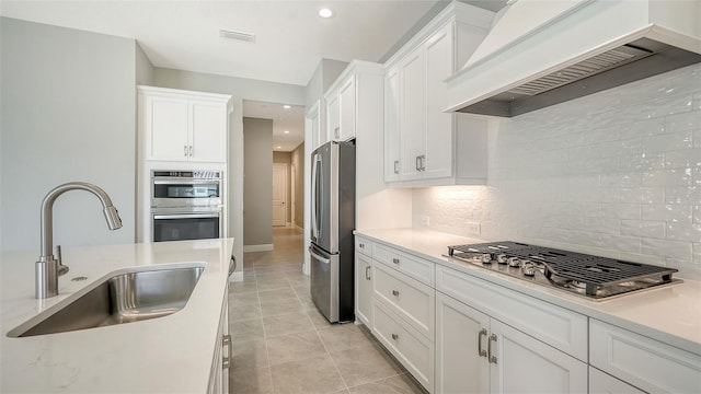 kitchen featuring white cabinetry, sink, custom range hood, and appliances with stainless steel finishes