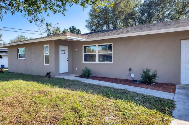 single story home with a shingled roof, a front yard, an attached garage, and stucco siding