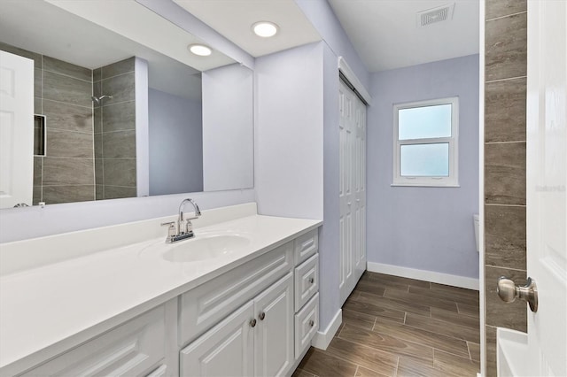 full bath featuring wood finish floors, visible vents, tiled shower, baseboards, and vanity