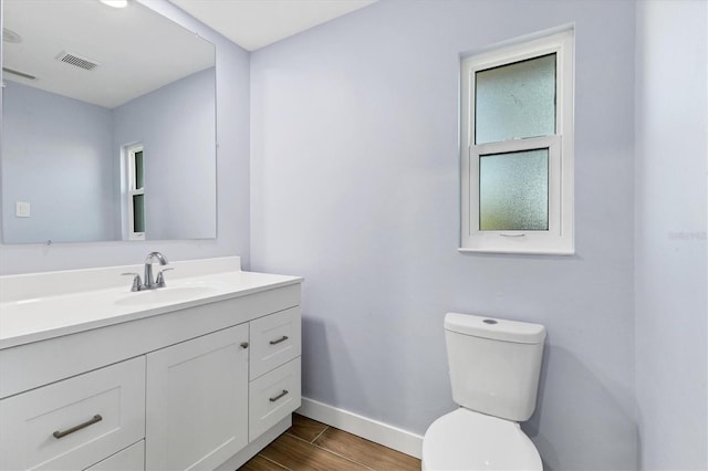 half bathroom with visible vents, toilet, wood finished floors, baseboards, and vanity