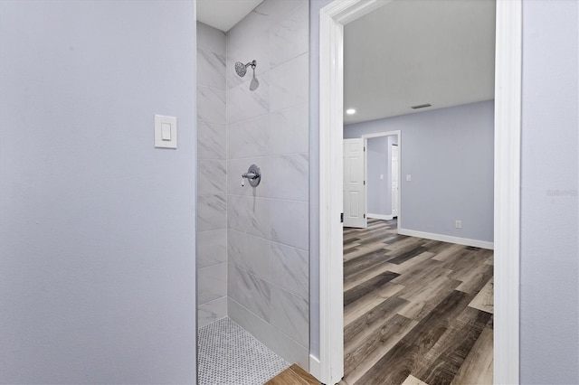 full bath with visible vents, tiled shower, baseboards, and wood finished floors