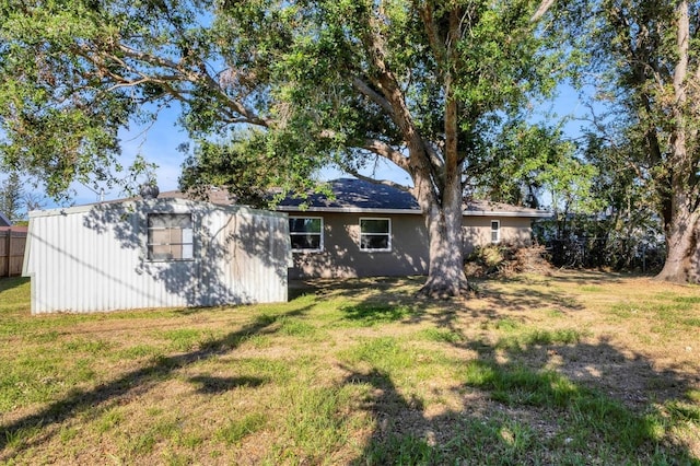 back of property featuring a lawn, an outdoor structure, and fence