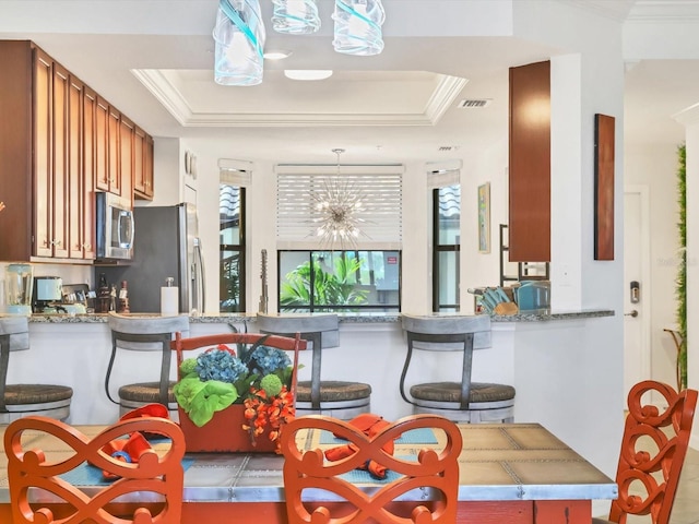 kitchen featuring kitchen peninsula, stainless steel appliances, a tray ceiling, pendant lighting, and a notable chandelier