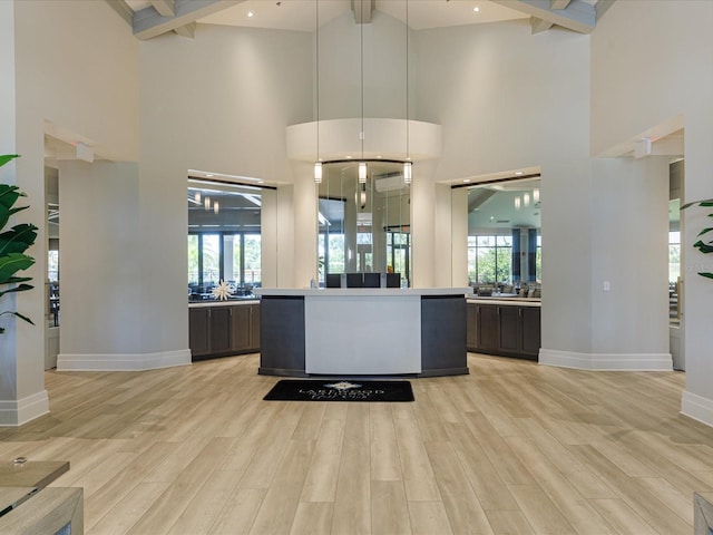 kitchen with beam ceiling, decorative light fixtures, a high ceiling, and light wood-type flooring