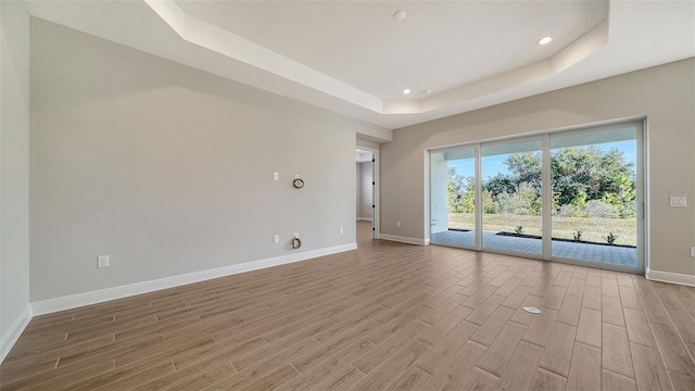 empty room with a raised ceiling and light wood-type flooring