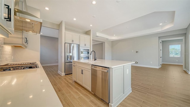 10142 Crystal Isles Cir, Sarasota, FL 34241 - kitchen featuring stainless steel appliances, light wood-style floors, a raised ceiling, an island with sink, and light countertops