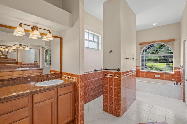 bathroom featuring a tub to relax in, a wealth of natural light, vanity, and tile walls