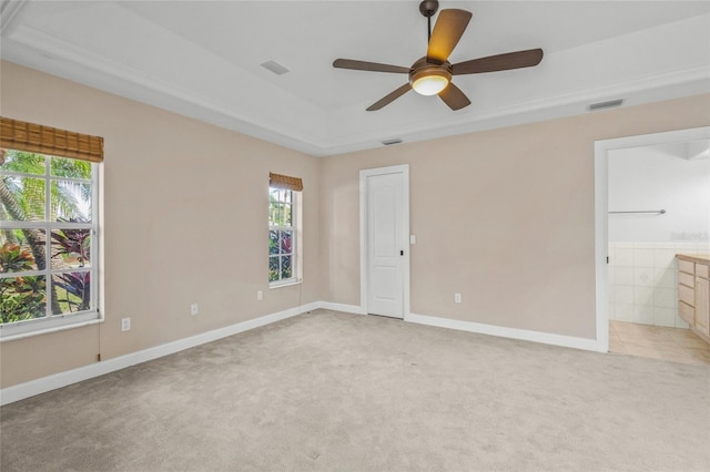 unfurnished bedroom with light carpet, connected bathroom, multiple windows, and ceiling fan