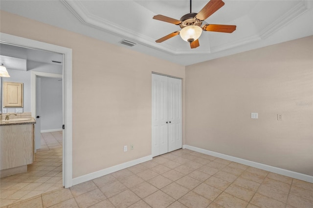 unfurnished bedroom featuring a tray ceiling, ceiling fan, crown molding, sink, and a closet