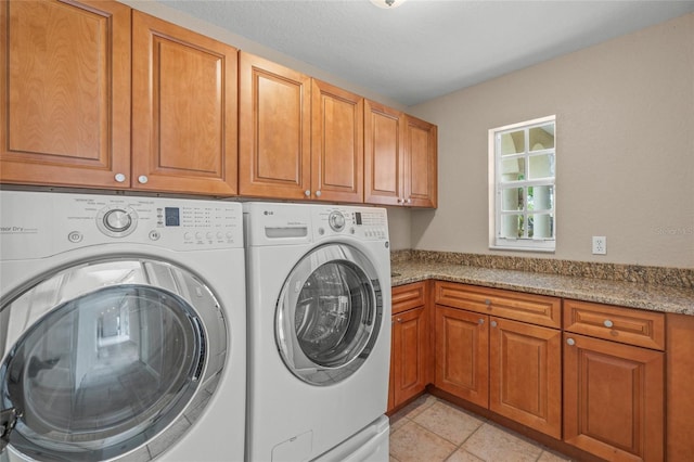 clothes washing area featuring washer and dryer, light tile patterned floors, and cabinets