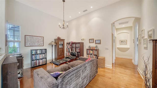 living room with light wood-type flooring, a high ceiling, and an inviting chandelier