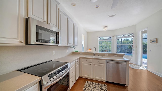 kitchen featuring kitchen peninsula, appliances with stainless steel finishes, sink, wood-type flooring, and white cabinets