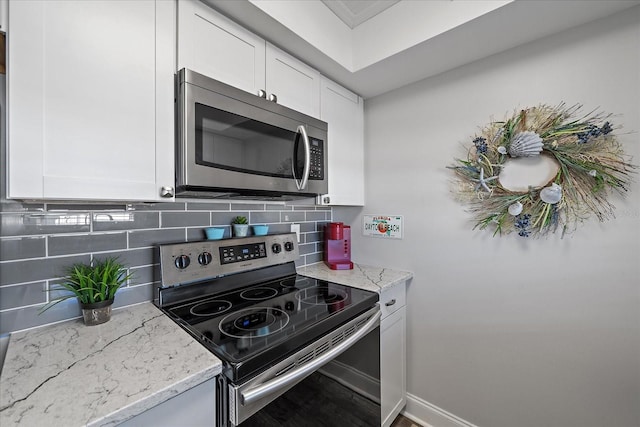 kitchen with tasteful backsplash, light stone counters, white cabinets, and appliances with stainless steel finishes