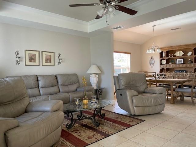 tiled living room with lofted ceiling, ceiling fan with notable chandelier, and ornamental molding