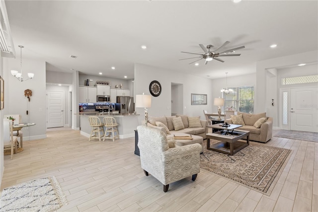 living area with recessed lighting, baseboards, light wood finished floors, and ceiling fan with notable chandelier