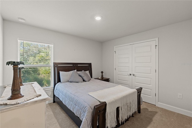 bedroom with baseboards, a closet, and light colored carpet