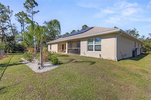 rear view of property with roof with shingles, stucco siding, a lawn, a sunroom, and roof mounted solar panels