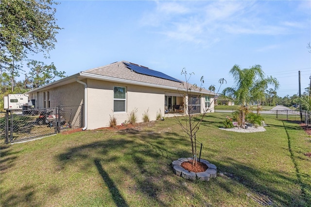 rear view of property with a shingled roof, fence, a lawn, roof mounted solar panels, and stucco siding