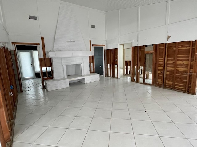 unfurnished living room with a towering ceiling, light tile patterned floors, and a brick fireplace