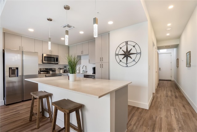 kitchen with hanging light fixtures, gray cabinets, appliances with stainless steel finishes, light hardwood / wood-style floors, and a breakfast bar area