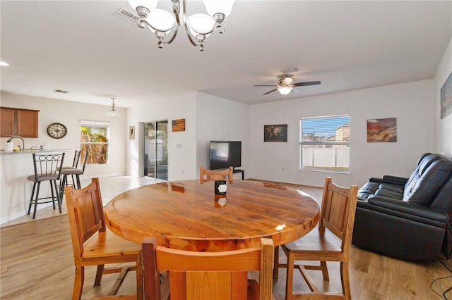 dining space featuring ceiling fan with notable chandelier, light hardwood / wood-style floors, and sink