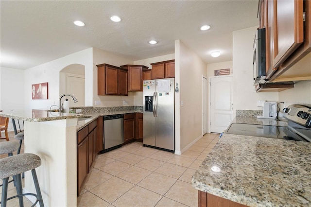 kitchen with light stone countertops, a kitchen bar, stainless steel appliances, and kitchen peninsula