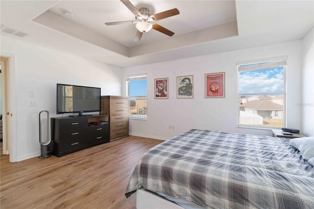 bedroom with ceiling fan, light hardwood / wood-style floors, and a raised ceiling