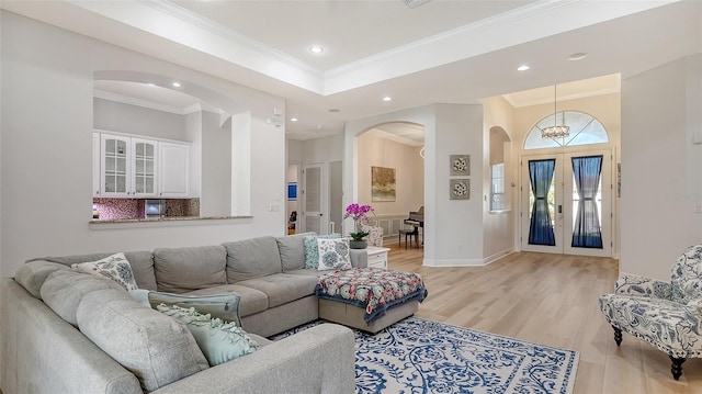 living room with a notable chandelier, light hardwood / wood-style floors, ornamental molding, and french doors