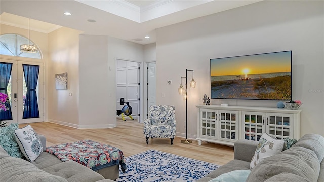 living room with a notable chandelier, light hardwood / wood-style floors, ornamental molding, and french doors