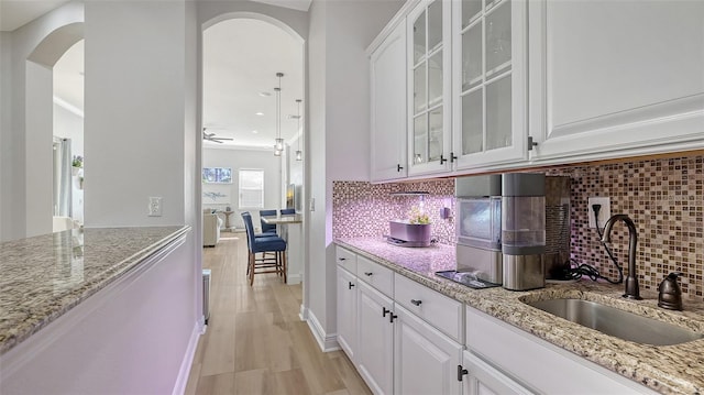 kitchen featuring light stone countertops, white cabinetry, sink, light hardwood / wood-style floors, and decorative backsplash