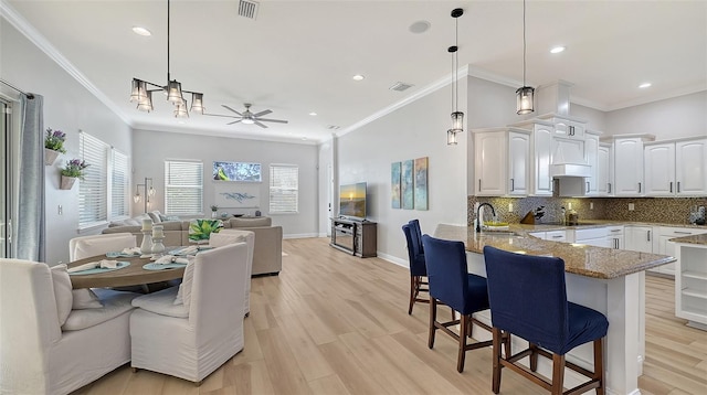 kitchen with a kitchen bar, kitchen peninsula, ceiling fan with notable chandelier, white cabinets, and hanging light fixtures