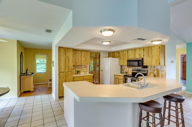 kitchen featuring kitchen peninsula, appliances with stainless steel finishes, a kitchen breakfast bar, a raised ceiling, and light tile patterned flooring