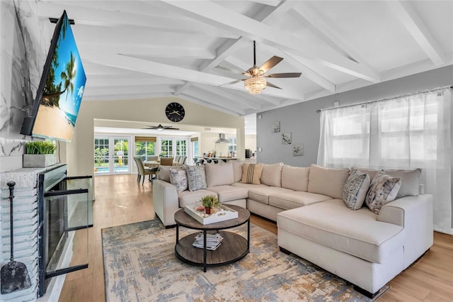 living room with light wood-type flooring, lofted ceiling with beams, a brick fireplace, and ceiling fan