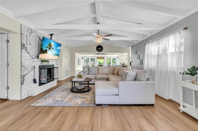 living room featuring vaulted ceiling with beams, ceiling fan, light hardwood / wood-style floors, and a brick fireplace