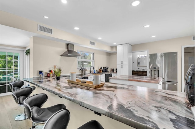 kitchen with wall chimney range hood, kitchen peninsula, a wealth of natural light, and high end refrigerator