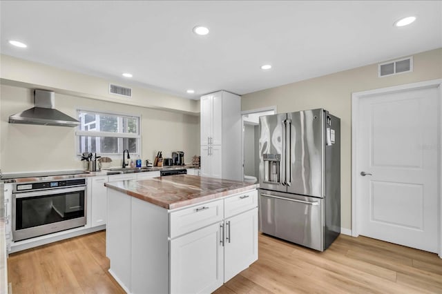 kitchen with light wood-type flooring, stainless steel appliances, white cabinetry, and wall chimney range hood