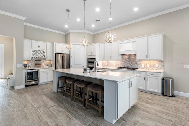 kitchen with premium range hood, white cabinets, an island with sink, stainless steel appliances, and beverage cooler