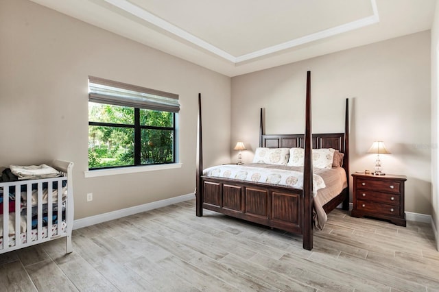 bedroom with light wood-type flooring and a tray ceiling