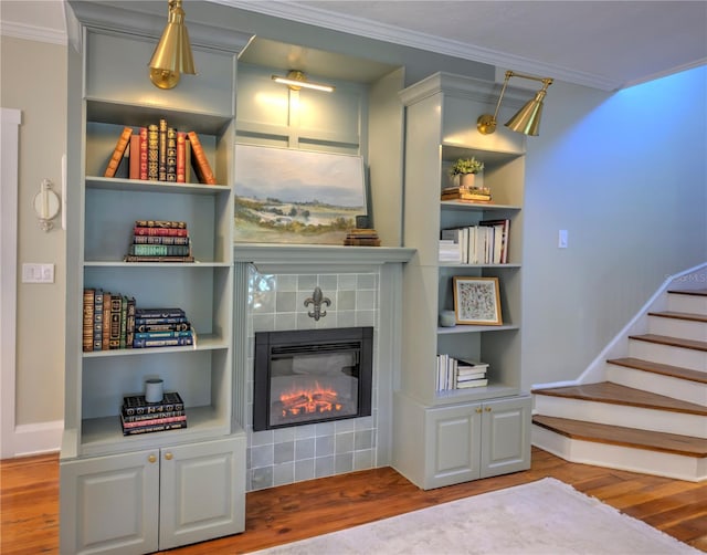 interior space with built in features, wood-type flooring, crown molding, and a tile fireplace