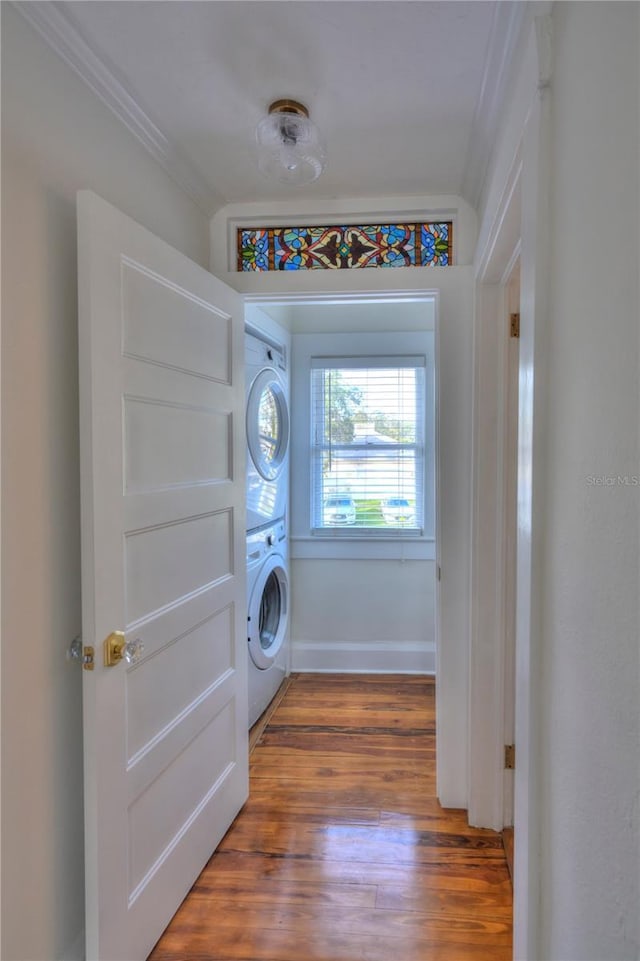 clothes washing area featuring wood-type flooring, stacked washer / dryer, and ornamental molding